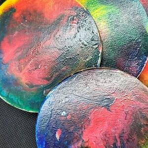May include: A set of circular coasters with abstract patterns. Each coaster displays a unique mix of colours, including red, blue, yellow, and green, producing a marbled appearance. The coasters are arranged in a slightly overlapping design.