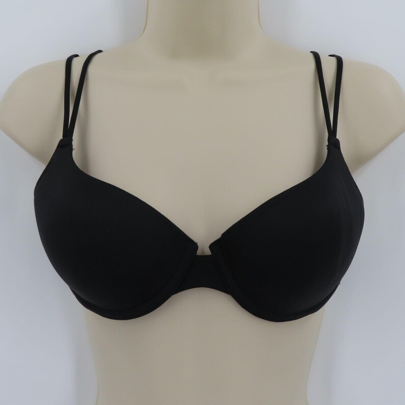 Op de afbeelding: Een zwarte bh met dunne, dubbele bandjes. De bh wordt getoond op een mannequin en heeft een klassiek beugelontwerp. De cups zijn glad en naadloos, wat een eenvoudige en elegante uitstraling geeft.