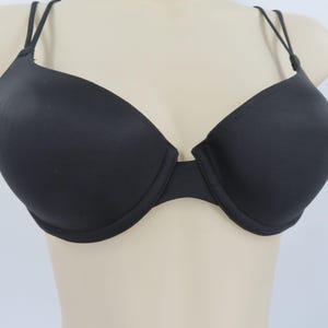 Op de afbeelding: Zwarte beha met beugel en dunne, verstelbare bandjes. De beha heeft een glad, naadloos ontwerp en een klassiek silhouet en biedt een comfortabele pasvorm. De beha wordt op een mannequin gepresenteerd.