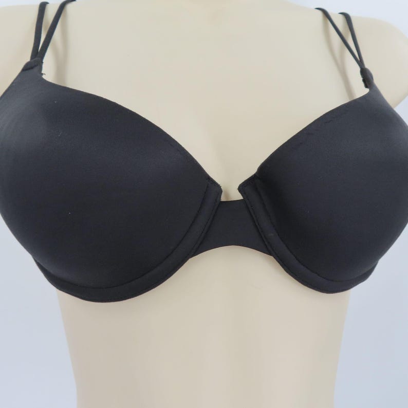 Op de afbeelding: Zwarte beha met beugel en dunne, verstelbare bandjes. De beha heeft een glad, naadloos ontwerp en een klassiek silhouet en biedt een comfortabele pasvorm. De beha wordt op een mannequin gepresenteerd.