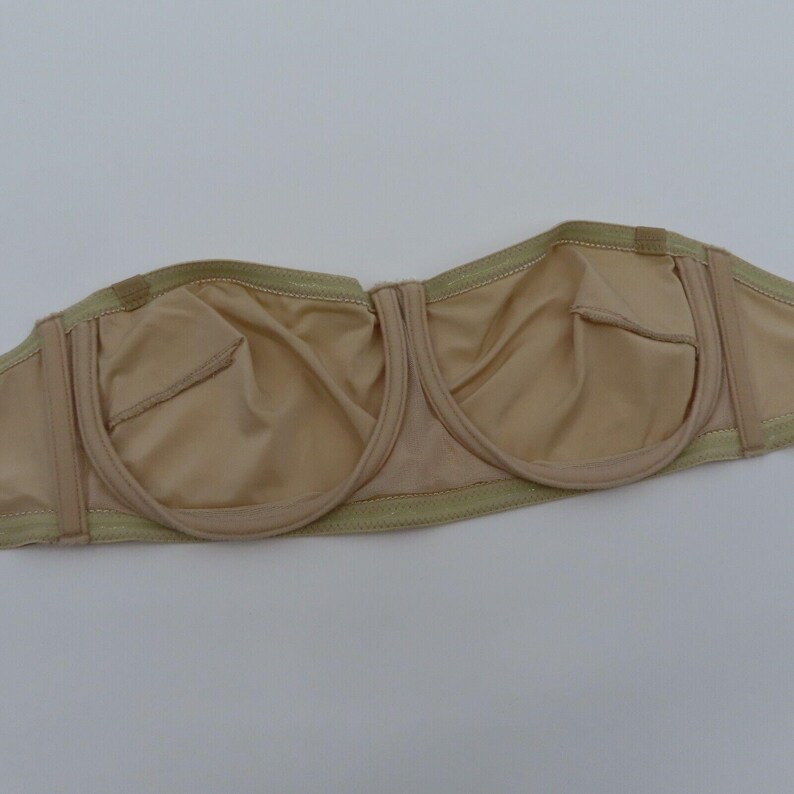 May include: A beige strapless bra with a smooth, seamless design. The bra features molded cups and a supportive underwire. The edges are trimmed with a light green fabric. The bra is designed for a comfortable and secure fit.