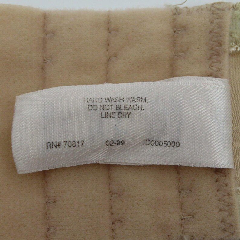 May include: A close-up of a beige fabric with a white tag. The tag reads "HAND WASH WARM. DO NOT BLEACH. LINE DRY." It also includes "RN# 70817", "02-99", and "ID0005000".