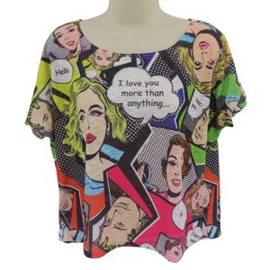 Puede incluir: Camiseta de manga corta y cuello redondo con diseño de cómic pop art. La camiseta está cubierta de ilustraciones coloridas de rostros de mujeres, bocadillos y el texto "I love you more than anything...".