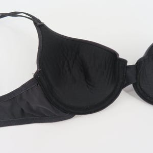 Op de afbeelding: Zwarte beha met verstelbare bandjes. De beha heeft voorgevormde cups en beugelondersteuning. De stof lijkt glad en licht glanzend. Deze beha is ontworpen voor dagelijks gebruik en biedt ondersteuning en bedekking.
