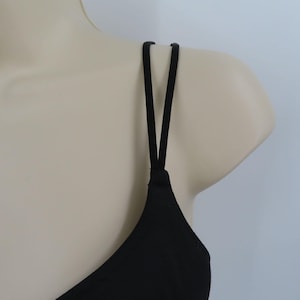 Op de afbeelding: Een zwarte camisole top met dunne spaghettibandjes. De bandjes zijn aan de schouders aan de top bevestigd en vormen een V. De top wordt op een mannequin getoond.