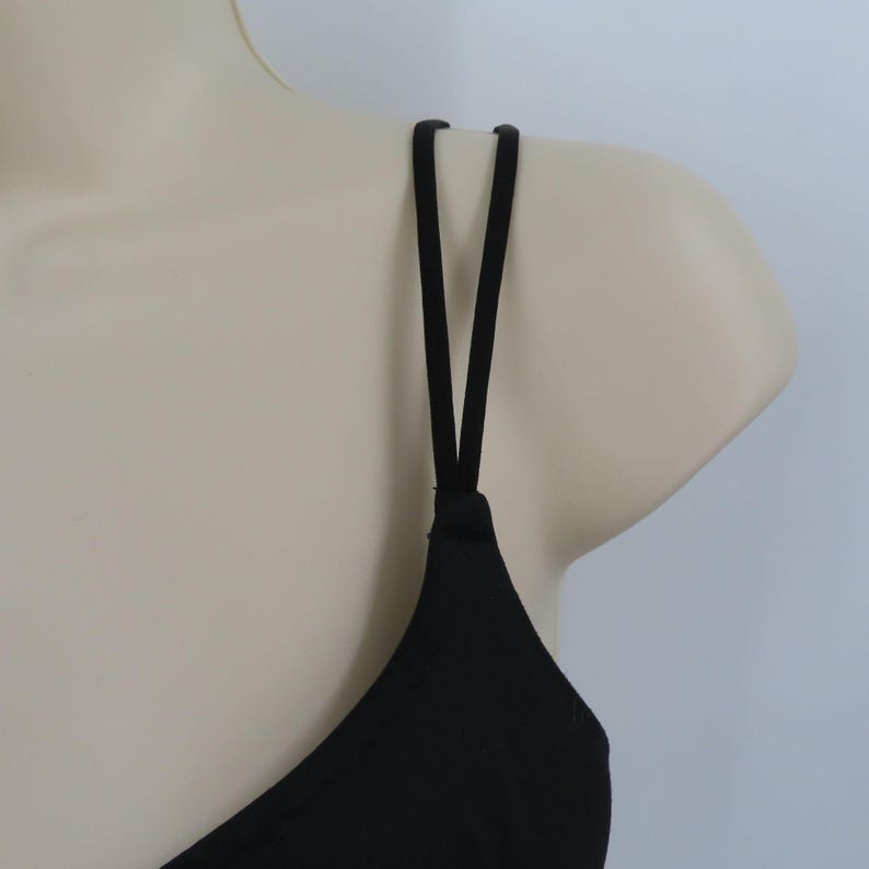 Op de afbeelding: Een zwarte camisole top met dunne spaghettibandjes. De bandjes zijn aan de schouders aan de top bevestigd en vormen een V. De top wordt op een mannequin getoond.