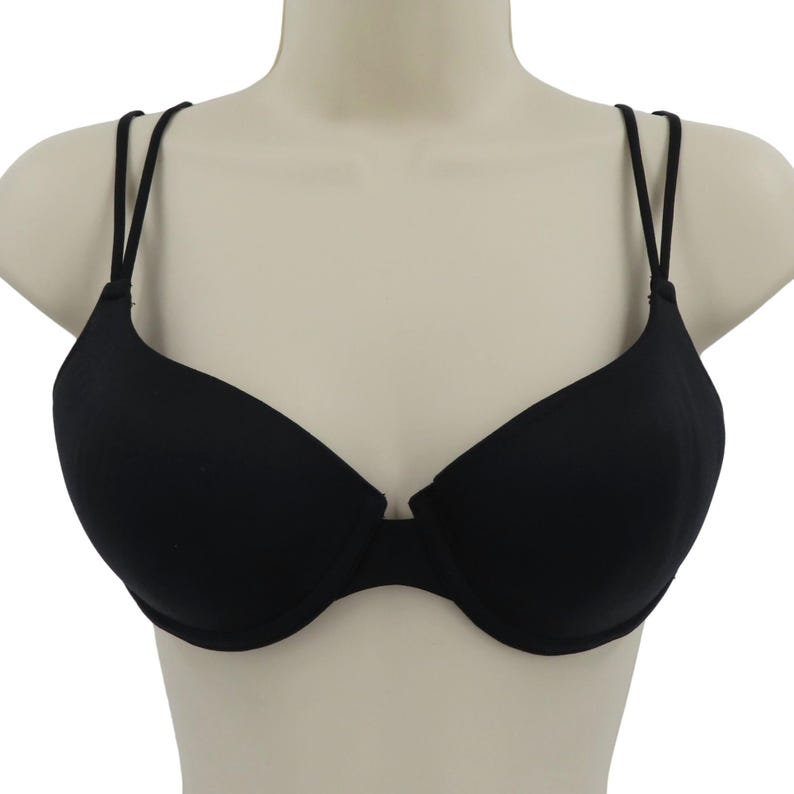 Op de afbeelding: Een zwarte beha met dunne, verstelbare bandjes. De beha heeft een klassiek ontwerp met voorgevormde cups en een lage middenvoor. De beha wordt op een mannequin getoond.