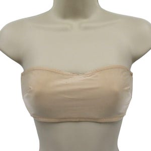 May include: A beige strapless bra displayed on a mannequin. The bra is made of a smooth fabric and features a scalloped top edge and a stitched hemline. The bra is designed to provide support without straps.