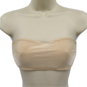 May include: A beige strapless bra made of a soft, seamless fabric. The bra has a curved neckline and is designed to provide support without straps. The edges are finished with a delicate stitch.