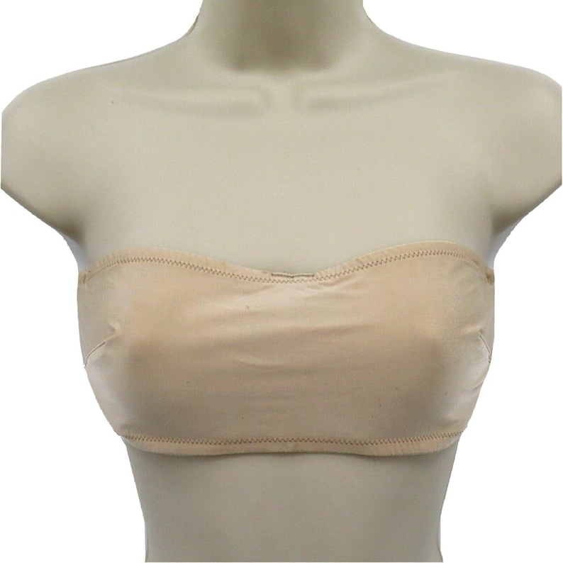 May include: A beige strapless bra made of a soft, seamless fabric. The bra has a curved neckline and is designed to provide support without straps. The edges are finished with a delicate stitch.