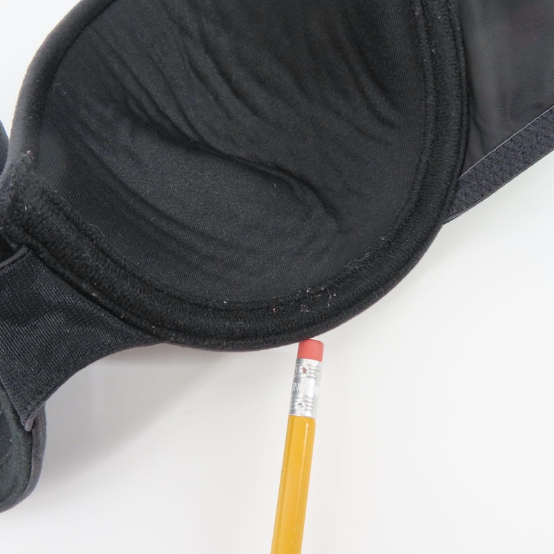 Op de afbeelding: Close-up van een zwarte bh met een voorgevormd cupontwerp. De bh heeft een gladde, matte afwerking en een gestructureerde vorm. Een gele potlood met een rode gum wordt naast de bh geplaatst voor de schaal.