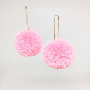 May include: A pair of pink pom-pom earrings with gold chain dangles.