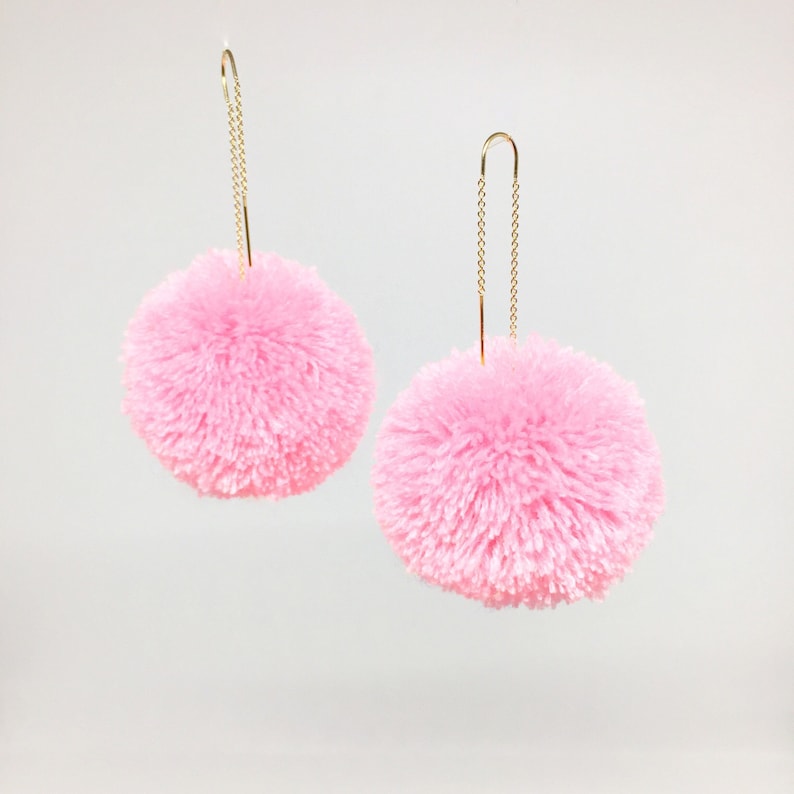 May include: A pair of pink pom-pom earrings with gold chain dangles.