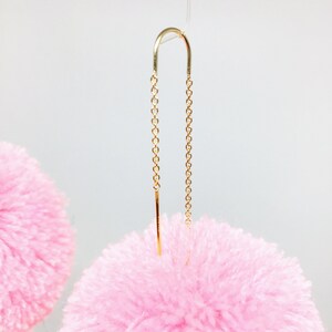 May include: A pair of pink fluffy pom-pom earrings with gold chain and bar dangles.