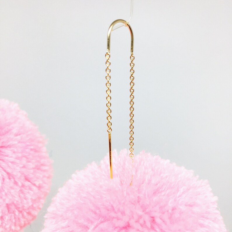 May include: A pair of pink fluffy pom-pom earrings with gold chain and bar dangles.