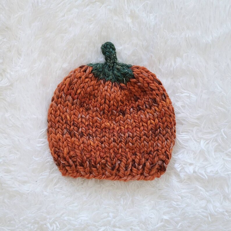 May include: A knitted pumpkin hat in orange and green. The hat is made with a chunky yarn and has a textured knit.