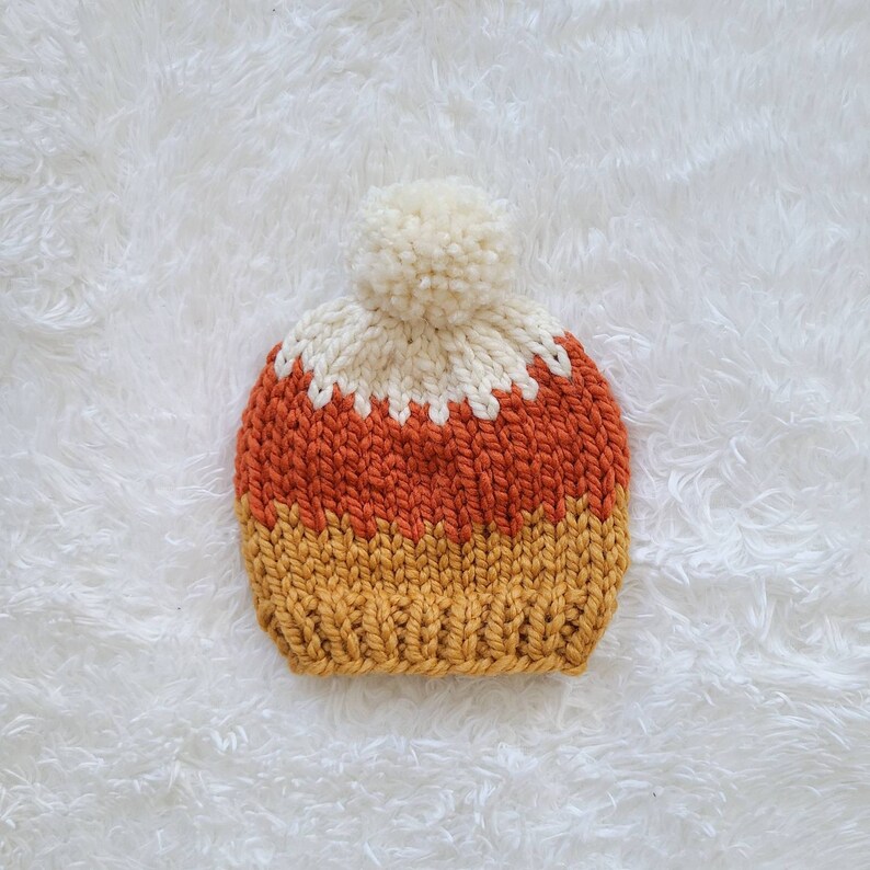 May include: A knitted hat with a white pom pom on top. The hat is striped with orange, white, and yellow.