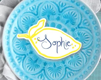 Może przedstawiać: Żółta karteczka do miejsca w kształcie cytryny z napisem "Sophie" napisanym niebieskim kursywą na niebieskim talerzu z wzorem.