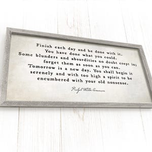 May include: A rectangular wooden sign with a gray frame. The sign features a quote in black text on a cream-colored background. The quote is attributed to Ralph Waldo Emerson.