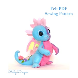 May include: A handmade felt baby dragon in shades of blue, pink, and purple. The dragon has large eyes, wings, and a curled tail adorned with flowers. Text on the image reads "Felt PDF Sewing Pattern" and "Baby Dragon".