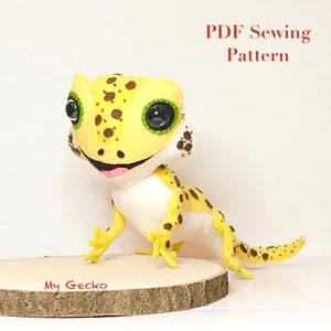 May include: A PDF sewing pattern for a yellow and brown gecko plush toy. The toy has large, black eyes with green pupils and a toothy grin. The pattern is titled "My Gecko" and is available as a digital download.