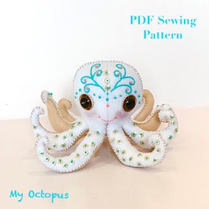 May include: A white felt octopus with embroidered details and gold sequins. The octopus has large brown eyes and a smiling mouth. The text "My Octopus" is printed below the octopus.