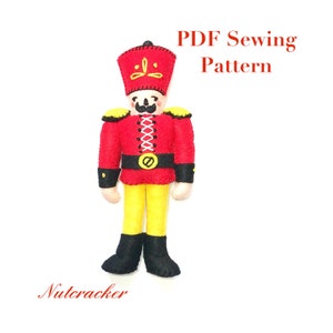 Può includere: Un modello di cucito in feltro per uno Schiaccianoci. Il modello è per uno Schiaccianoci rosso e giallo con un cappello e stivali neri. Il modello include il testo "PDF Sewing Pattern".