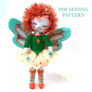 May include: A handmade fairy doll with a white face, closed eyes, and red hair. The doll wears a green top, a yellow skirt, and orange boots. It has blue wings and is decorated with small blue flowers. The text "PDF SEWING PATTERN" is visible.