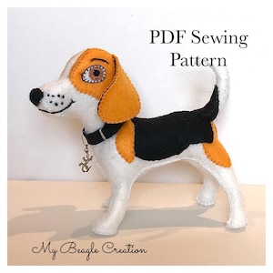 May include: A PDF sewing pattern for a felt beagle dog toy. The dog is white with black and orange patches. It has a black collar with a gold charm.