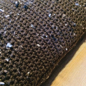 May include: Close-up of a brown knitted pillow with white flecks throughout the fabric.