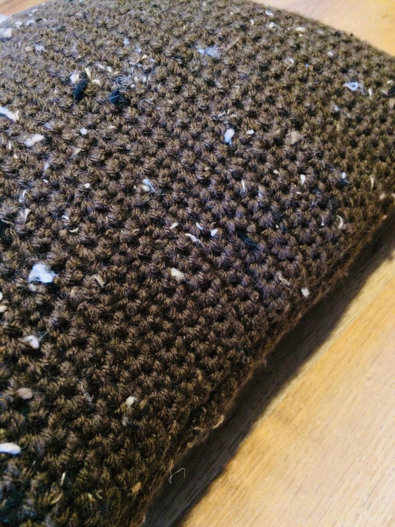 May include: Close-up of a brown knitted pillow with white flecks throughout the fabric.