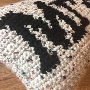 May include: A white and black crocheted pillow with a geometric pattern. The pillow is made with a speckled yarn.