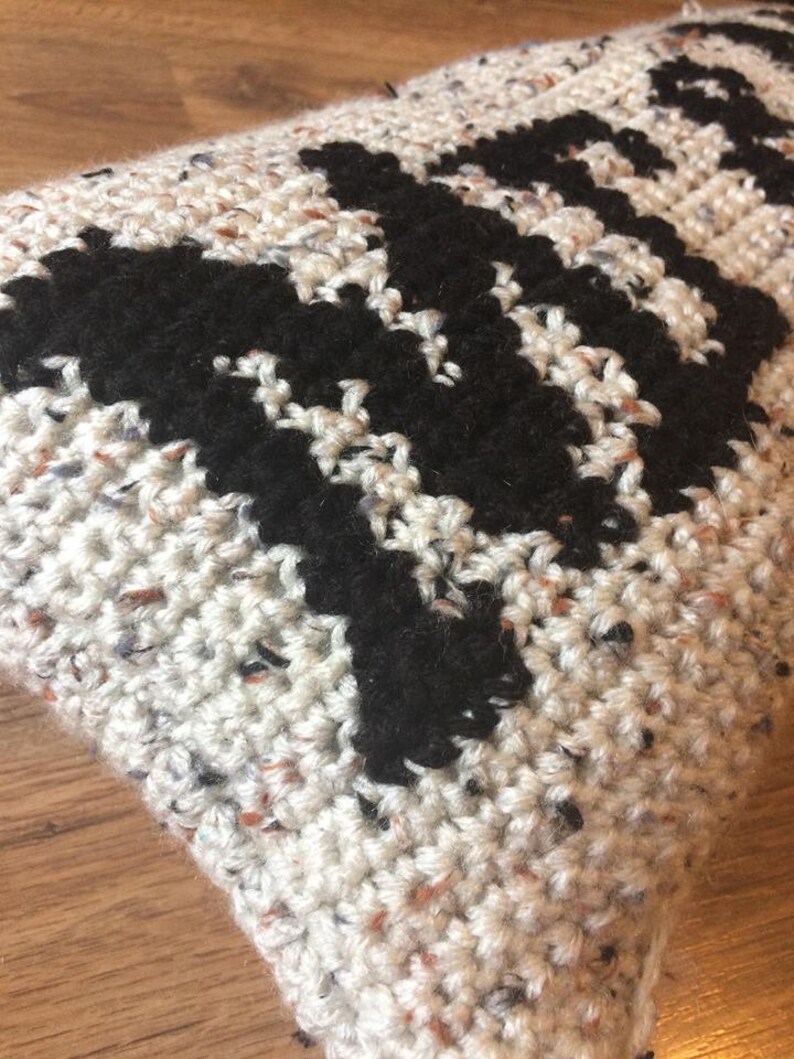 May include: A white and black crocheted pillow with a geometric pattern. The pillow is made with a speckled yarn.