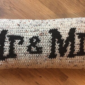 May include: A long, rectangular pillow with a white and gray speckled fabric. The pillow has the words "Mr. & Mrs." embroidered in black.