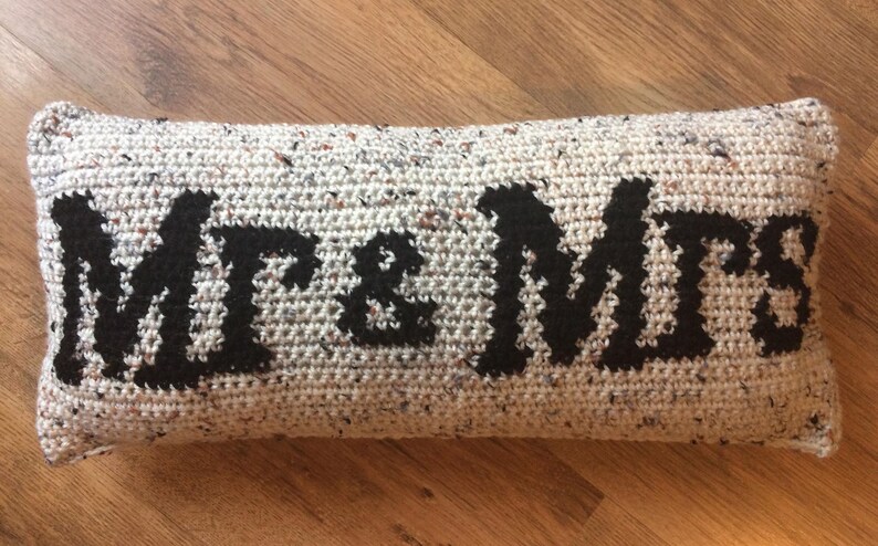 May include: A long, rectangular pillow with a white and gray speckled fabric. The pillow has the words "Mr. & Mrs." embroidered in black.
