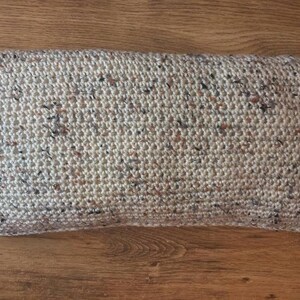 May include: A beige crocheted pillow with a speckled pattern of brown, white, and black yarn.