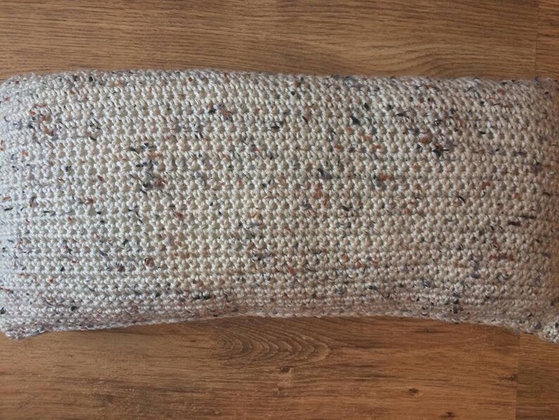 May include: A beige crocheted pillow with a speckled pattern of brown, white, and black yarn.