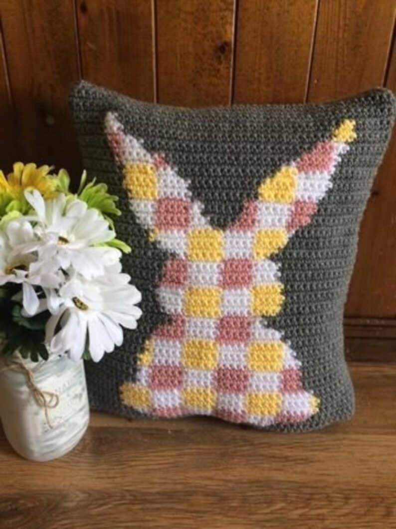 May include: A gray crocheted pillow with a pink and yellow checkered bunny design.