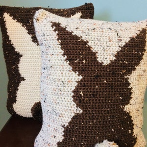 May include: Two crocheted pillows with a brown and white chevron pattern. One pillow has a brown pom-pom on the bottom.