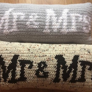 May include: Two crocheted pillows with different designs. The top pillow is gray with the word "LOVE" in white. The bottom pillow is beige with the words "Mr. & Mrs." in black.