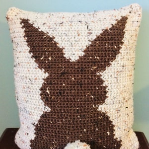 May include: A white and brown crocheted pillow with a bunny silhouette and a white pom-pom tail.