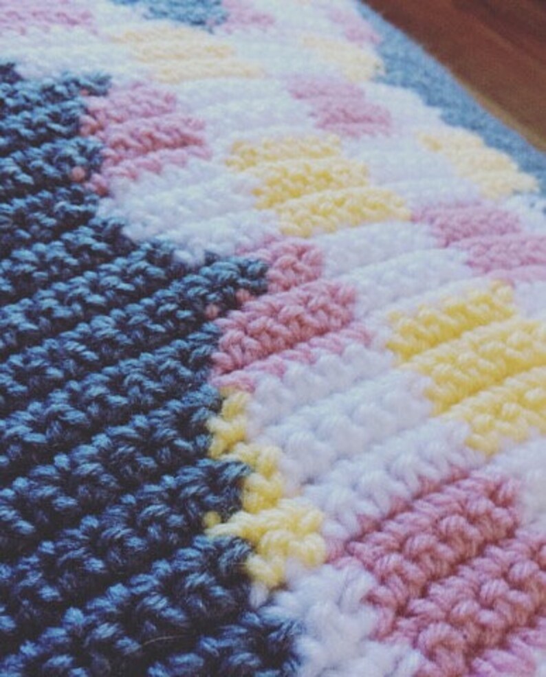 May include: Close-up of a knitted blanket with a blue, pink, white, and yellow color pattern.