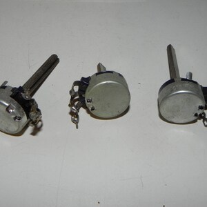May include: Three silver potentiometers with black knobs and metal shafts. The potentiometers have three terminals each.