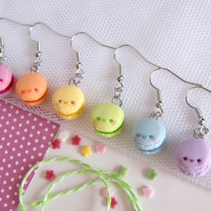 Könnte beinhalten: Regenbogen-Macaron-Ohrringe mit süßen Gesichtern. Die Macarons sind rosa, orange, gelb, grün, blau und lila.