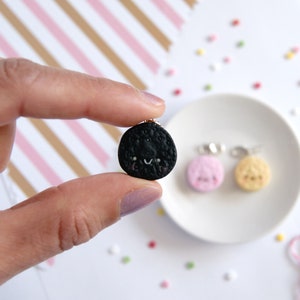 Op de afbeelding: Een set van drie miniatuur koekjescharms in zwart, wit en roze, elk met een vrolijk gezicht. De charms zijn gemaakt van polymer clay en hebben een glanzende afwerking.
