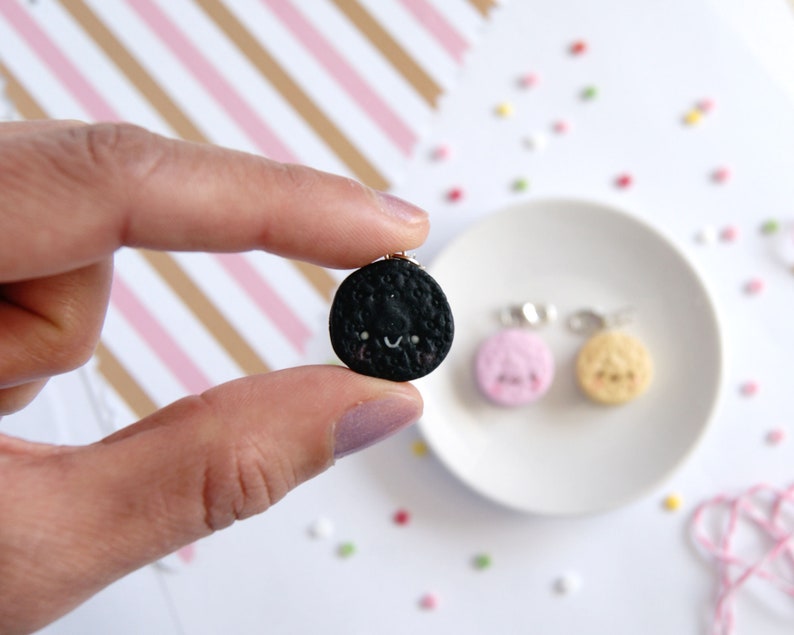 Op de afbeelding: Een set van drie miniatuur koekjescharms in zwart, wit en roze, elk met een vrolijk gezicht. De charms zijn gemaakt van polymer clay en hebben een glanzende afwerking.