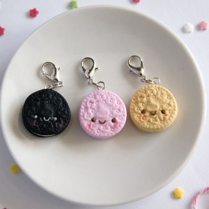 Op de afbeelding: Drie bedelarmen in de vorm van koekjes met blije gezichtjes. De koekjes zijn zwart, roze en geel.