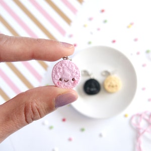 Op de afbeelding: Een roze klei-hanger in de vorm van een koekje met een glimlachend gezicht. De hanger is bevestigd aan een zilveren ketting.