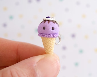 May include: A purple ice cream cone charm with a white swirl and a chocolate drizzle. The cone is made of yellow polymer clay and has a textured surface.