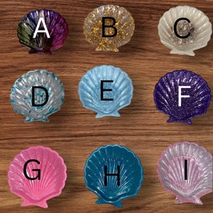 May include: Nine decorative seashell-shaped dishes with different colors and glitter finishes. The dishes are labeled A through I.